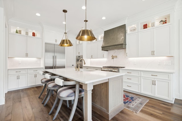 kitchen featuring custom exhaust hood, a center island with sink, tasteful backsplash, pendant lighting, and white cabinets