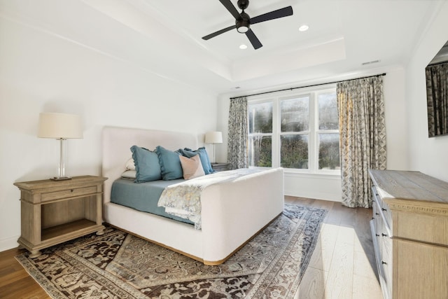 bedroom with ceiling fan, light wood-type flooring, and a raised ceiling