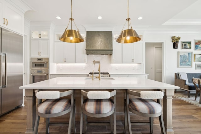 kitchen with appliances with stainless steel finishes, custom exhaust hood, decorative backsplash, and a center island with sink