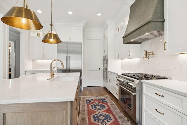 kitchen featuring premium range hood, white cabinets, a center island with sink, and stainless steel appliances