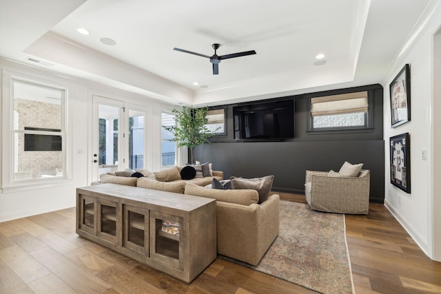 living room with ceiling fan, a tray ceiling, and hardwood / wood-style flooring