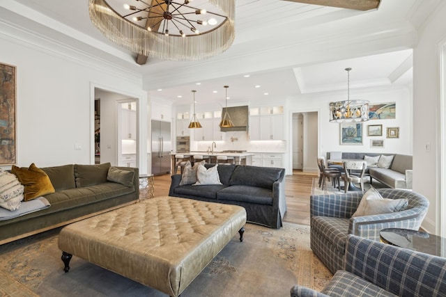 living room featuring sink, crown molding, an inviting chandelier, a tray ceiling, and hardwood / wood-style flooring