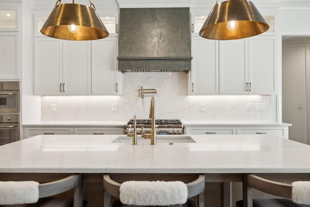 kitchen with a breakfast bar area, a kitchen island with sink, white cabinets, and custom range hood