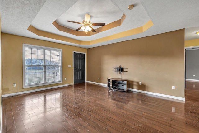 interior space with a textured ceiling, a raised ceiling, ceiling fan, and dark wood-type flooring