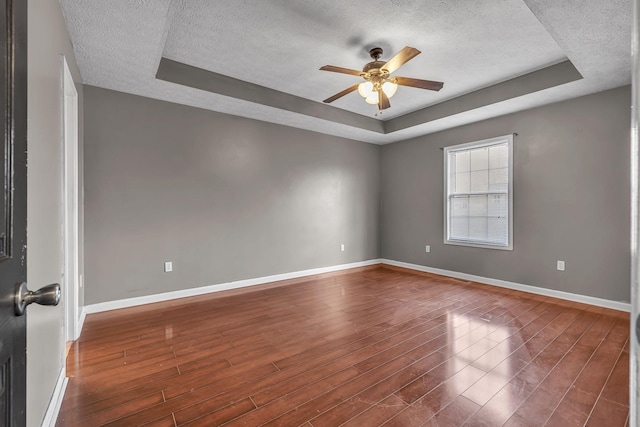 spare room with ceiling fan, dark hardwood / wood-style flooring, a textured ceiling, and a tray ceiling