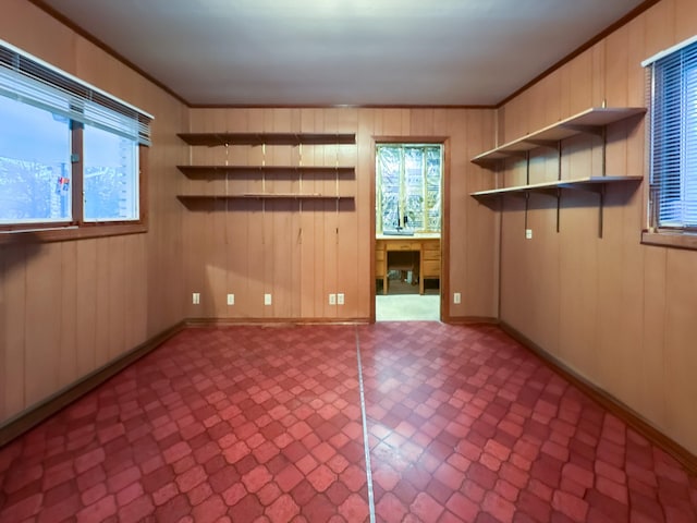 unfurnished room with crown molding, wooden walls, and built in desk