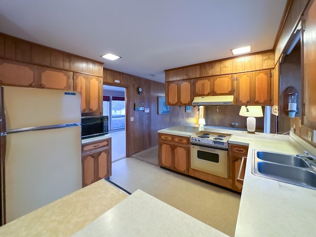 kitchen with white electric range, sink, wood walls, refrigerator, and oven