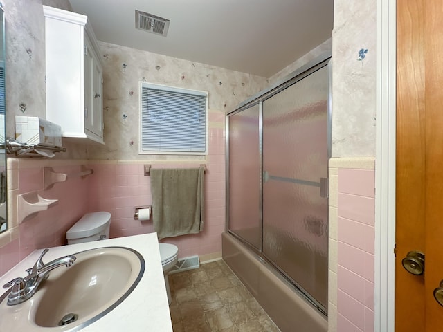 full bathroom with toilet, vanity, bath / shower combo with glass door, and tile walls