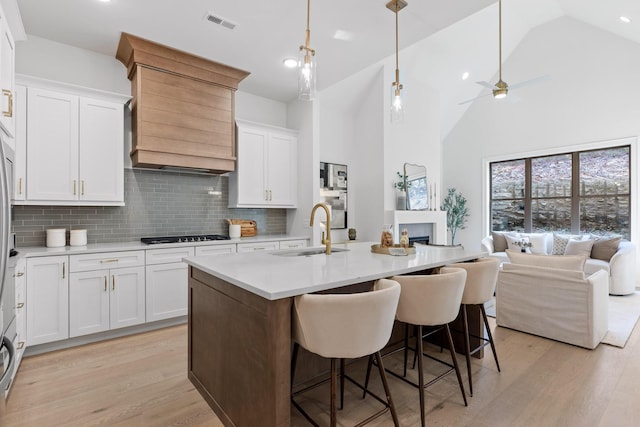 kitchen featuring white cabinets, backsplash, a center island with sink, and sink