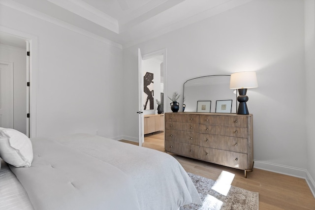 bedroom with a tray ceiling, ensuite bathroom, light hardwood / wood-style floors, and ornamental molding