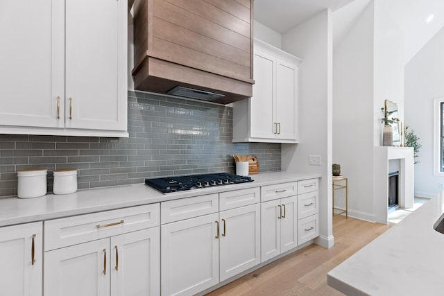 kitchen with backsplash, light wood-type flooring, custom range hood, white cabinetry, and gas cooktop