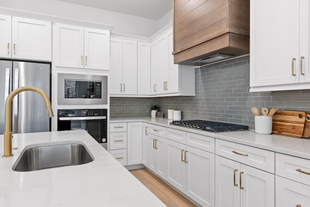 kitchen featuring backsplash, stainless steel appliances, white cabinetry, and premium range hood