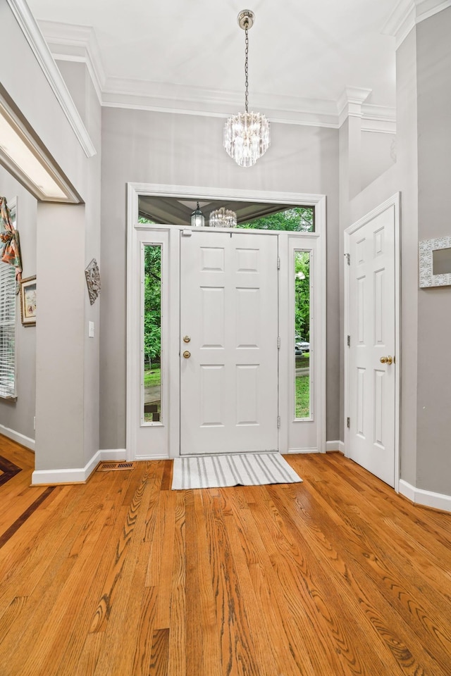 entryway featuring light wood-type flooring, ornamental molding, and a chandelier