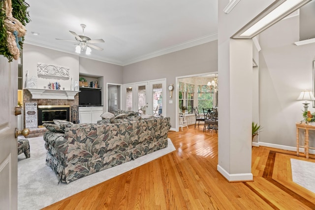 living room featuring ceiling fan, french doors, a brick fireplace, crown molding, and light hardwood / wood-style floors