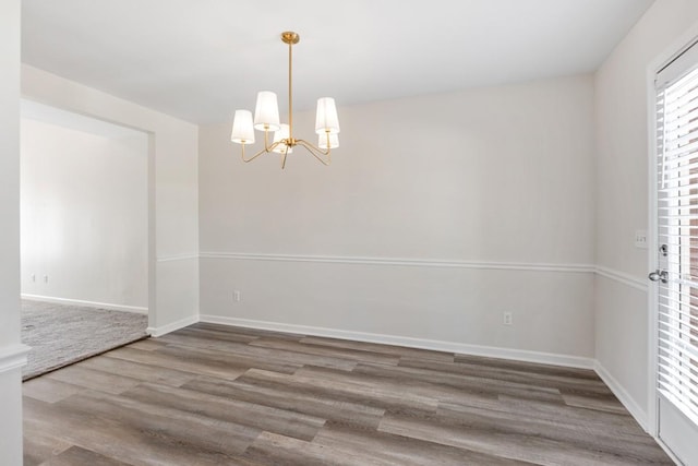 empty room with wood-type flooring and an inviting chandelier