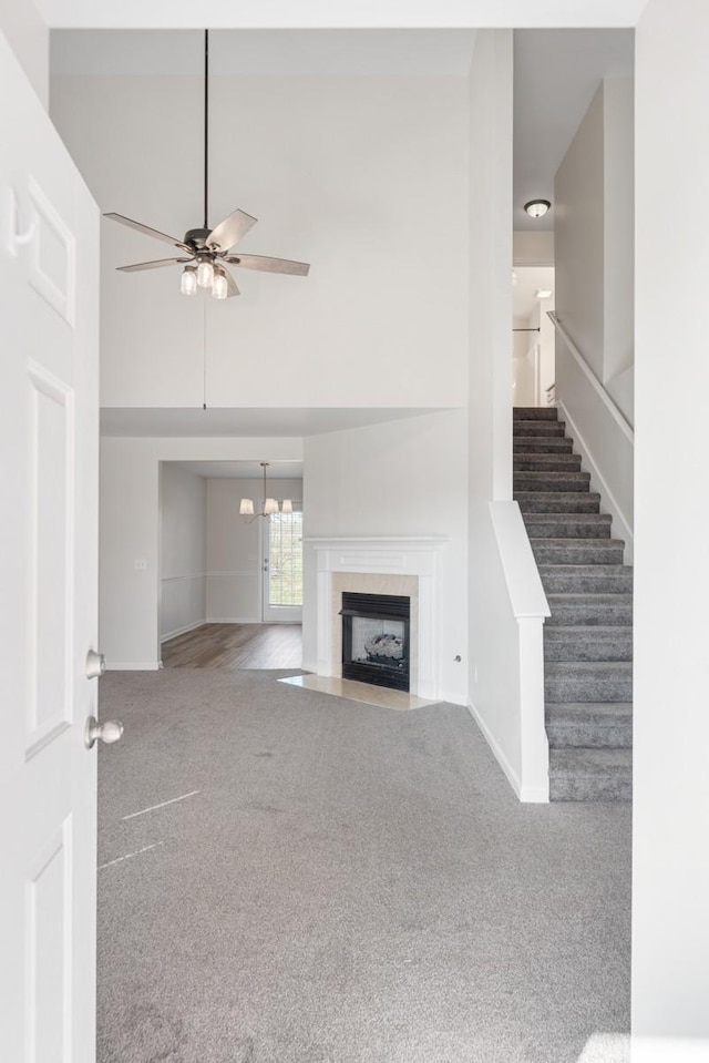 unfurnished living room featuring carpet, a high ceiling, and ceiling fan with notable chandelier