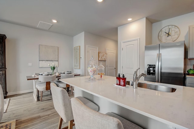 kitchen with a kitchen breakfast bar, sink, light stone countertops, light wood-type flooring, and stainless steel fridge with ice dispenser