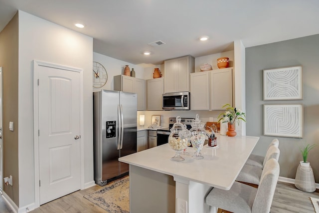 kitchen featuring kitchen peninsula, light wood-type flooring, a breakfast bar, stainless steel appliances, and gray cabinets