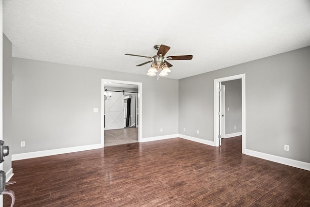 spare room featuring ceiling fan, a barn door, dark hardwood / wood-style flooring, and a textured ceiling