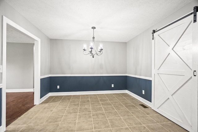 unfurnished dining area with tile patterned flooring, a textured ceiling, a barn door, and a notable chandelier