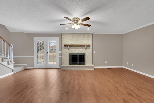 unfurnished living room with hardwood / wood-style floors, french doors, a brick fireplace, ceiling fan, and ornamental molding