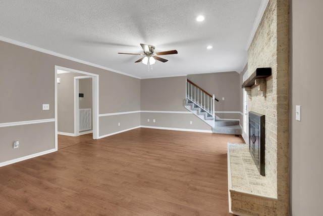 unfurnished living room featuring a stone fireplace, crown molding, ceiling fan, a textured ceiling, and wood-type flooring