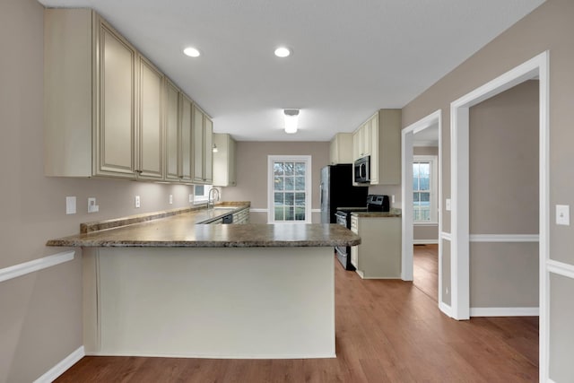 kitchen with kitchen peninsula, appliances with stainless steel finishes, sink, cream cabinets, and light hardwood / wood-style flooring