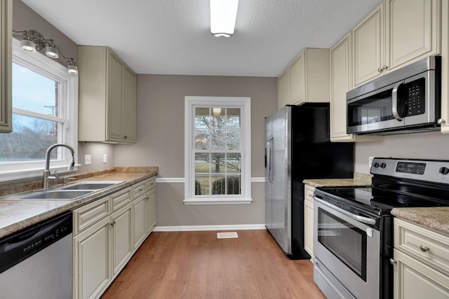 kitchen featuring sink, stainless steel appliances, a textured ceiling, cream cabinetry, and light wood-type flooring