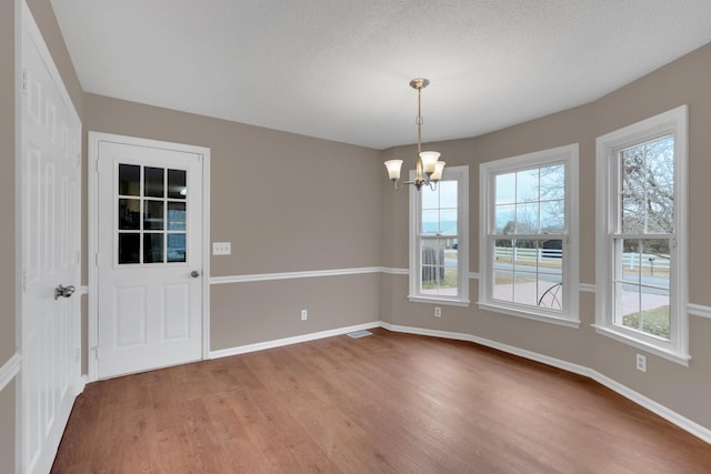 unfurnished dining area featuring plenty of natural light, wood-type flooring, a textured ceiling, and a chandelier