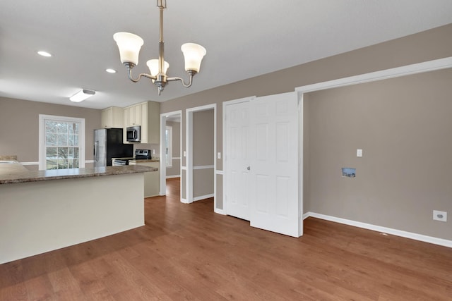 kitchen featuring dark wood-type flooring, an inviting chandelier, dark stone countertops, decorative light fixtures, and appliances with stainless steel finishes