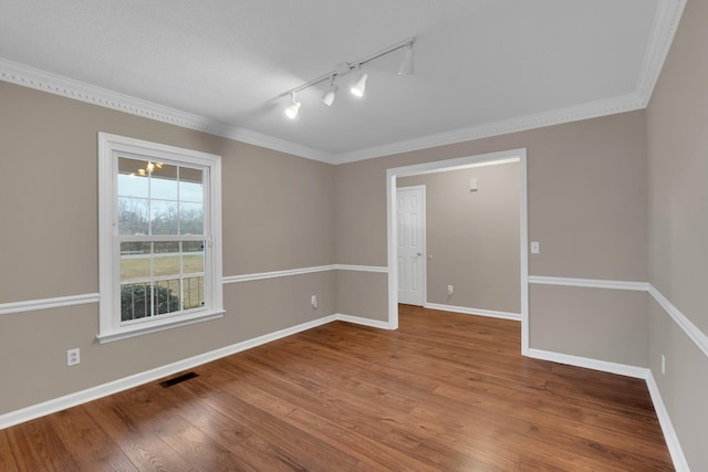 empty room with hardwood / wood-style floors, crown molding, and track lighting