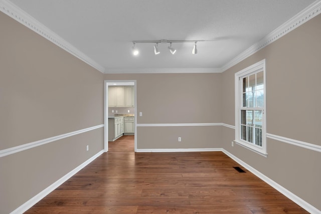 empty room featuring hardwood / wood-style floors, rail lighting, and ornamental molding