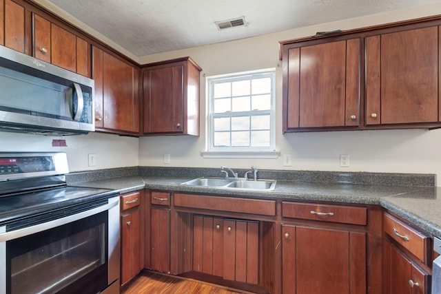 kitchen with wood-type flooring, appliances with stainless steel finishes, a textured ceiling, and sink