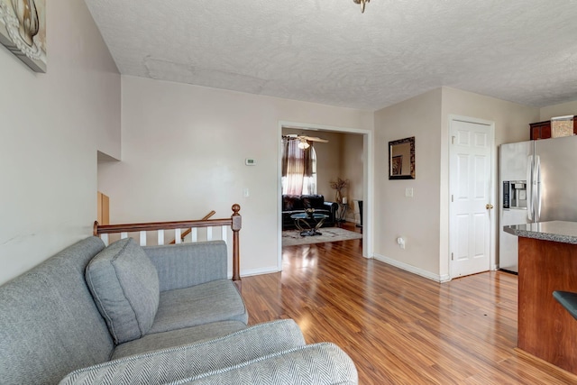 living room featuring ceiling fan, light hardwood / wood-style floors, and a textured ceiling