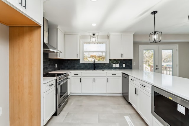 kitchen featuring appliances with stainless steel finishes, french doors, wall chimney range hood, sink, and decorative light fixtures