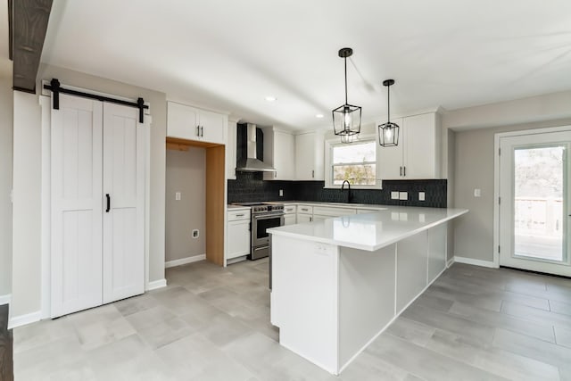 kitchen with wall chimney range hood, a barn door, decorative light fixtures, stainless steel electric stove, and white cabinets