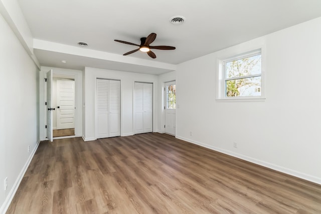 unfurnished bedroom featuring multiple closets, ceiling fan, and dark wood-type flooring