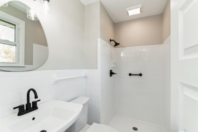 bathroom with toilet, sink, a tile shower, and tile walls