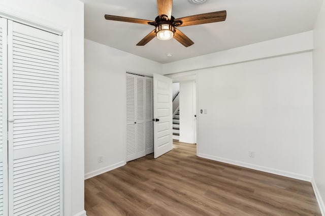 unfurnished bedroom with dark hardwood / wood-style floors, ceiling fan, and multiple closets