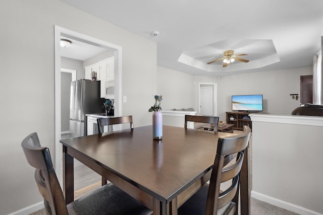 dining space with ceiling fan, a raised ceiling, and carpet flooring