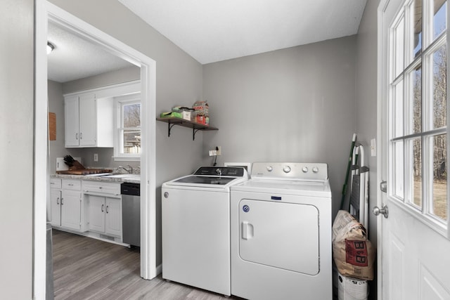 laundry area with sink, light wood-type flooring, washing machine and clothes dryer, and plenty of natural light