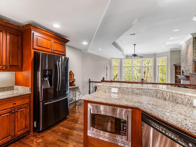 kitchen featuring light stone countertops, ceiling fan, dark wood-type flooring, appliances with stainless steel finishes, and ornamental molding