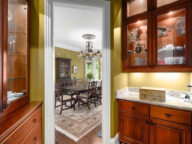 bar featuring hardwood / wood-style floors, a notable chandelier, light stone counters, and crown molding