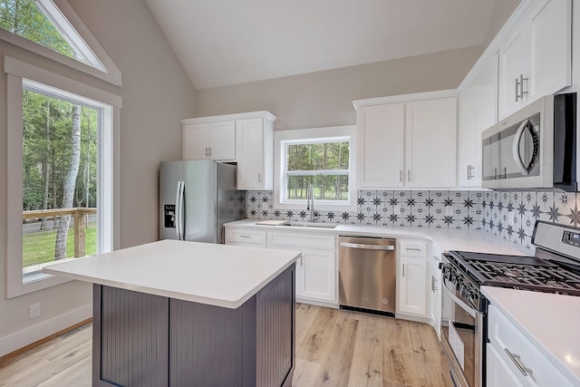 kitchen featuring a center island, vaulted ceiling, decorative backsplash, white cabinets, and appliances with stainless steel finishes