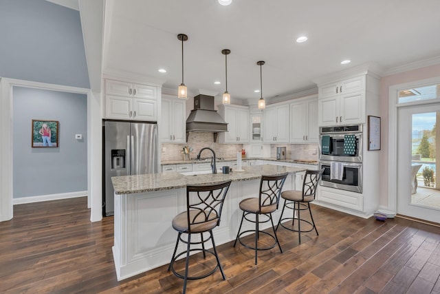 kitchen featuring pendant lighting, premium range hood, light stone countertops, white cabinetry, and stainless steel appliances