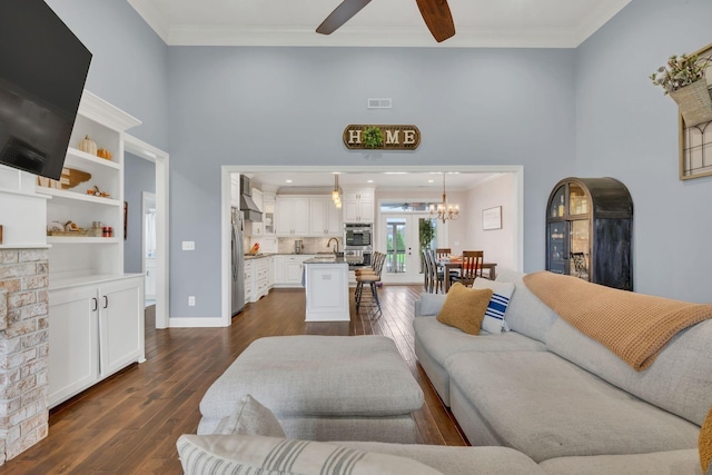 living room with ceiling fan with notable chandelier, crown molding, dark wood-type flooring, and sink