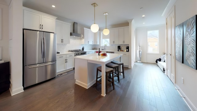 kitchen featuring a center island, white cabinets, wall chimney range hood, decorative light fixtures, and stainless steel appliances