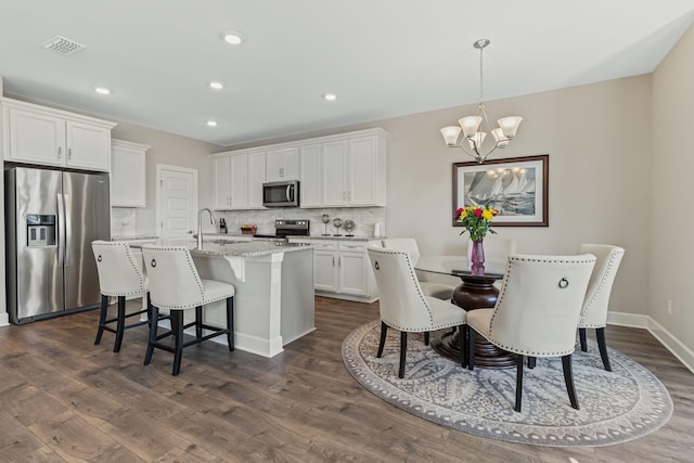 kitchen featuring white cabinetry, hanging light fixtures, a chandelier, a kitchen island with sink, and appliances with stainless steel finishes