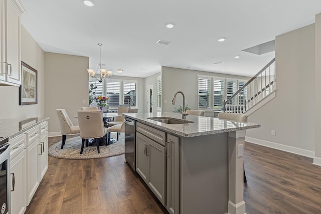 kitchen with light stone countertops, a center island with sink, stainless steel dishwasher, and sink