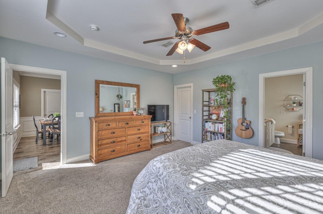 bedroom with light carpet, ensuite bath, a raised ceiling, and ceiling fan